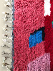 Close-up of the Timlilit Moroccan rug showing red, pink, and blue wool textures with fringe.