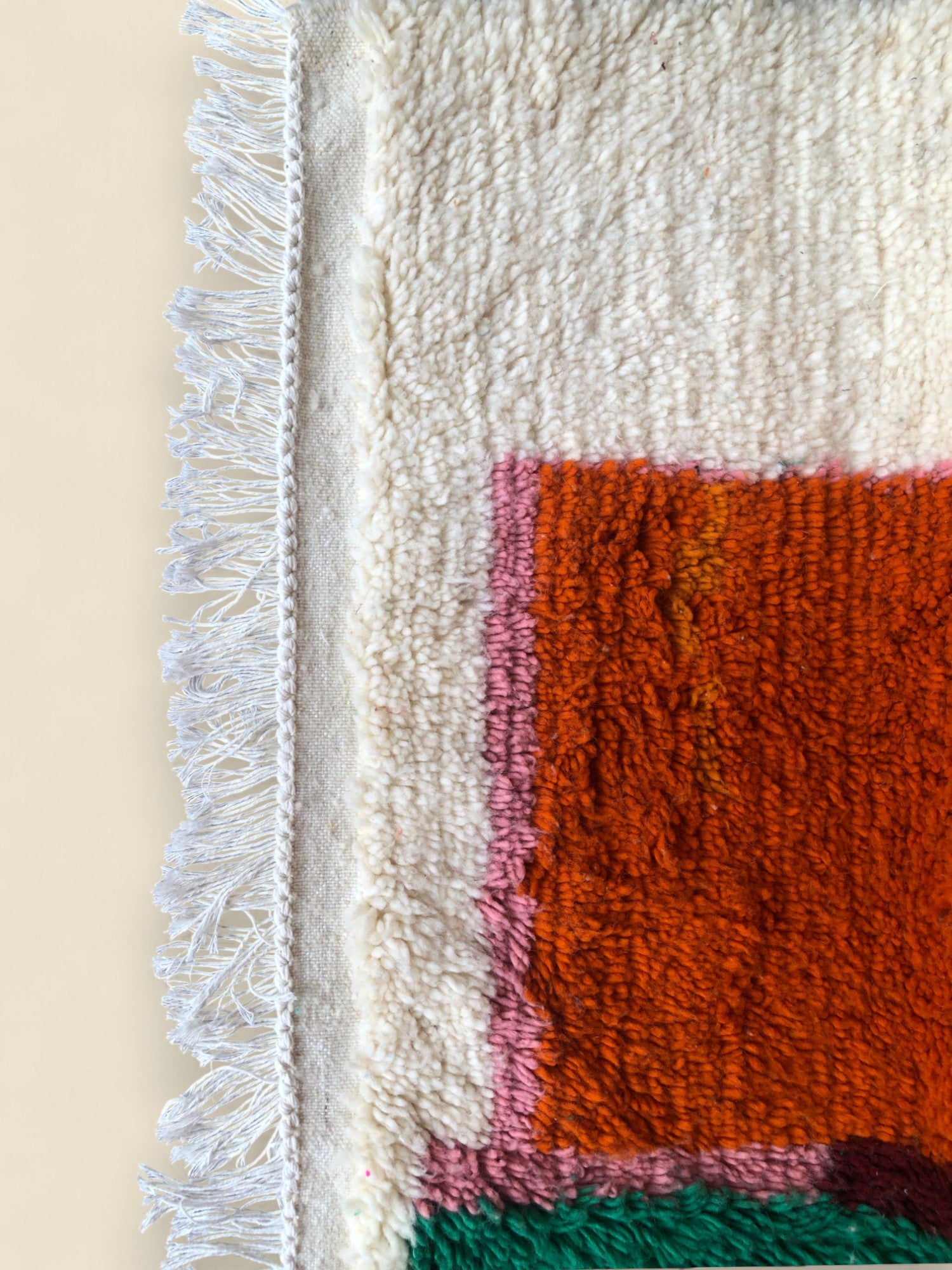 Corner of a Berber rug showing white fringe and orange color block