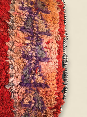 Close-up of hand-knotted wool texture in red, purple, peach, and orange tones on a Moroccan pouffe.