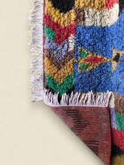 Corner of Tazdayt rug with fringe and bold colors on tile floor.