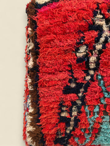 Close-up of a colorful textured fabric with red, black, and multicolor patterns on a beige background.