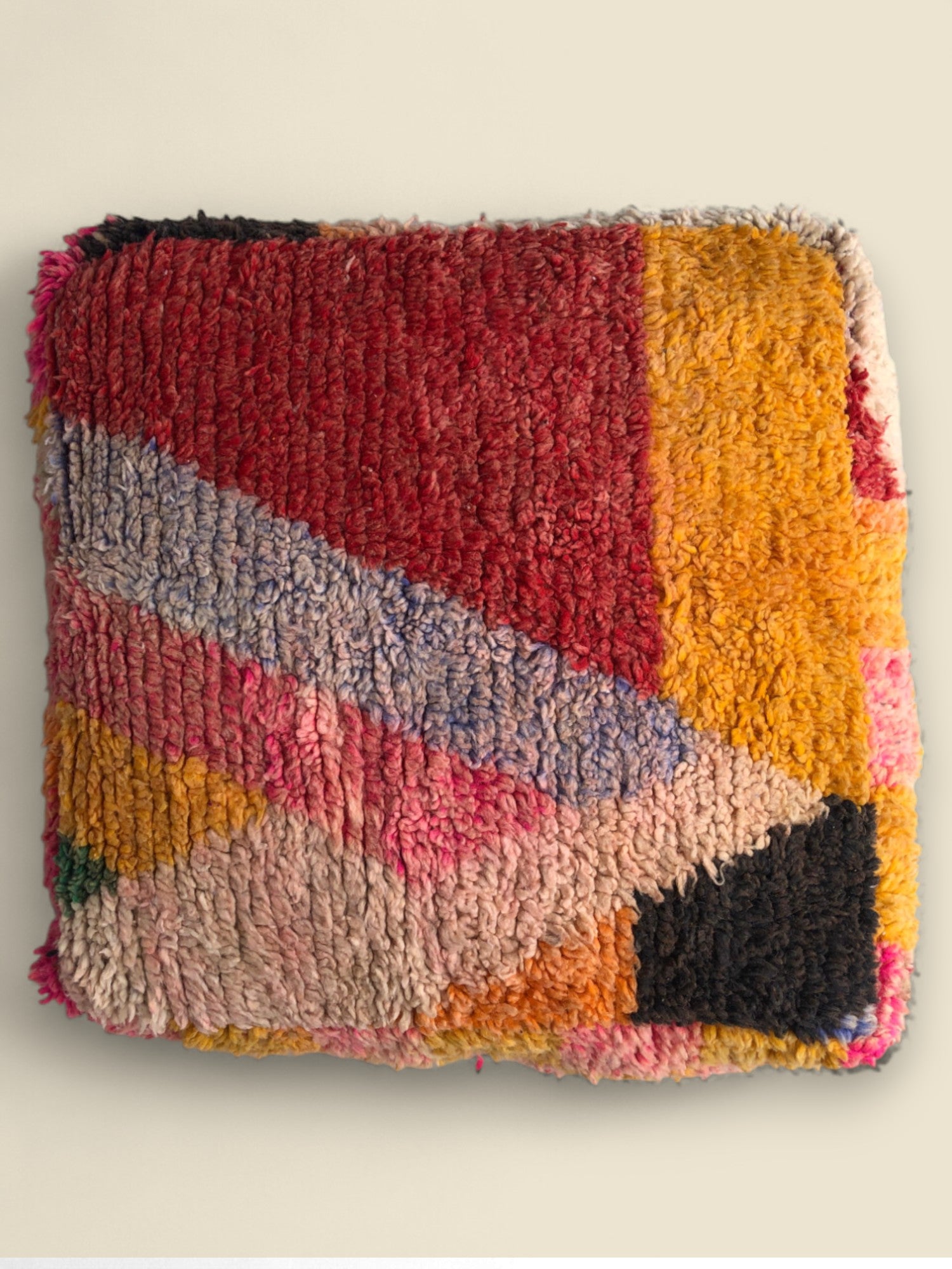 Colorful Tawenza Moroccan pouffe with geometric wool patterns in red, yellow, and pink tones