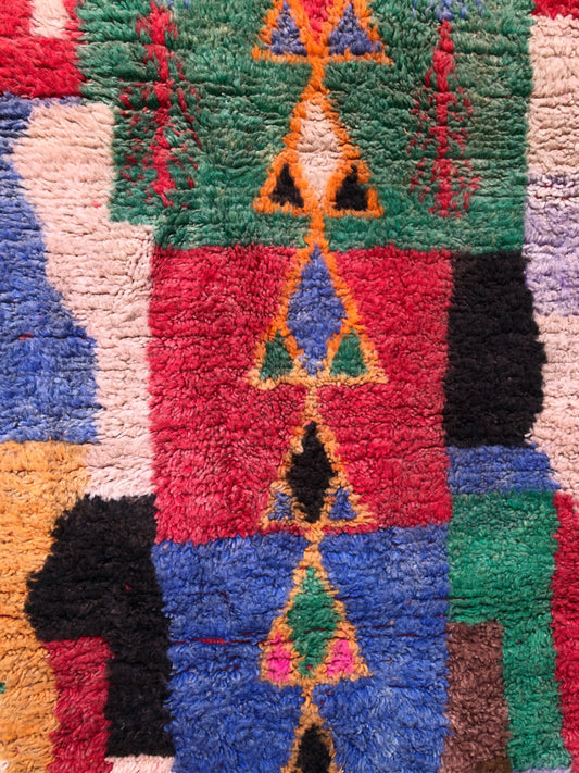 Geometric triangle motifs on red and green Tazdayt rug background.