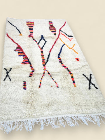 Moroccan wool rug with colorful patterns laid flat on a wooden floor.
