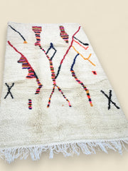 Moroccan wool rug with colorful patterns laid flat on a wooden floor.