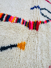 Close-up of the Tazla Moroccan rug showing colorful wool patterns on a cream base