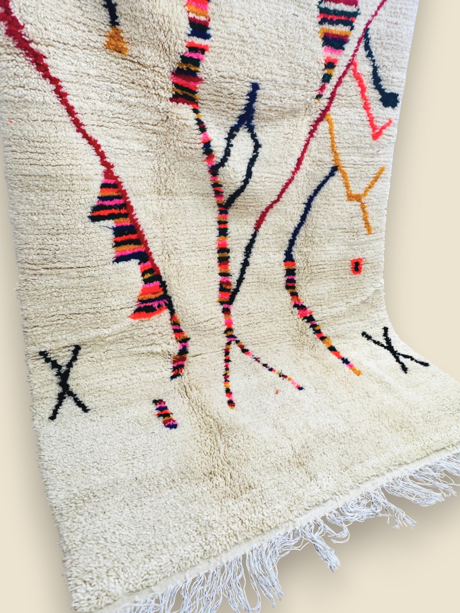 Handwoven Moroccan rug with vibrant abstract lines displayed against a white wall.