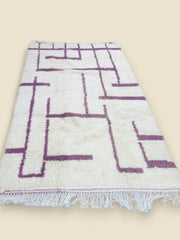 Handwoven Berber carpet displayed on wooden floor with mauve pattern