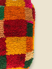 Colorful wool Moroccan pouffe in Tirga patchwork pattern with red, green, and orange squares