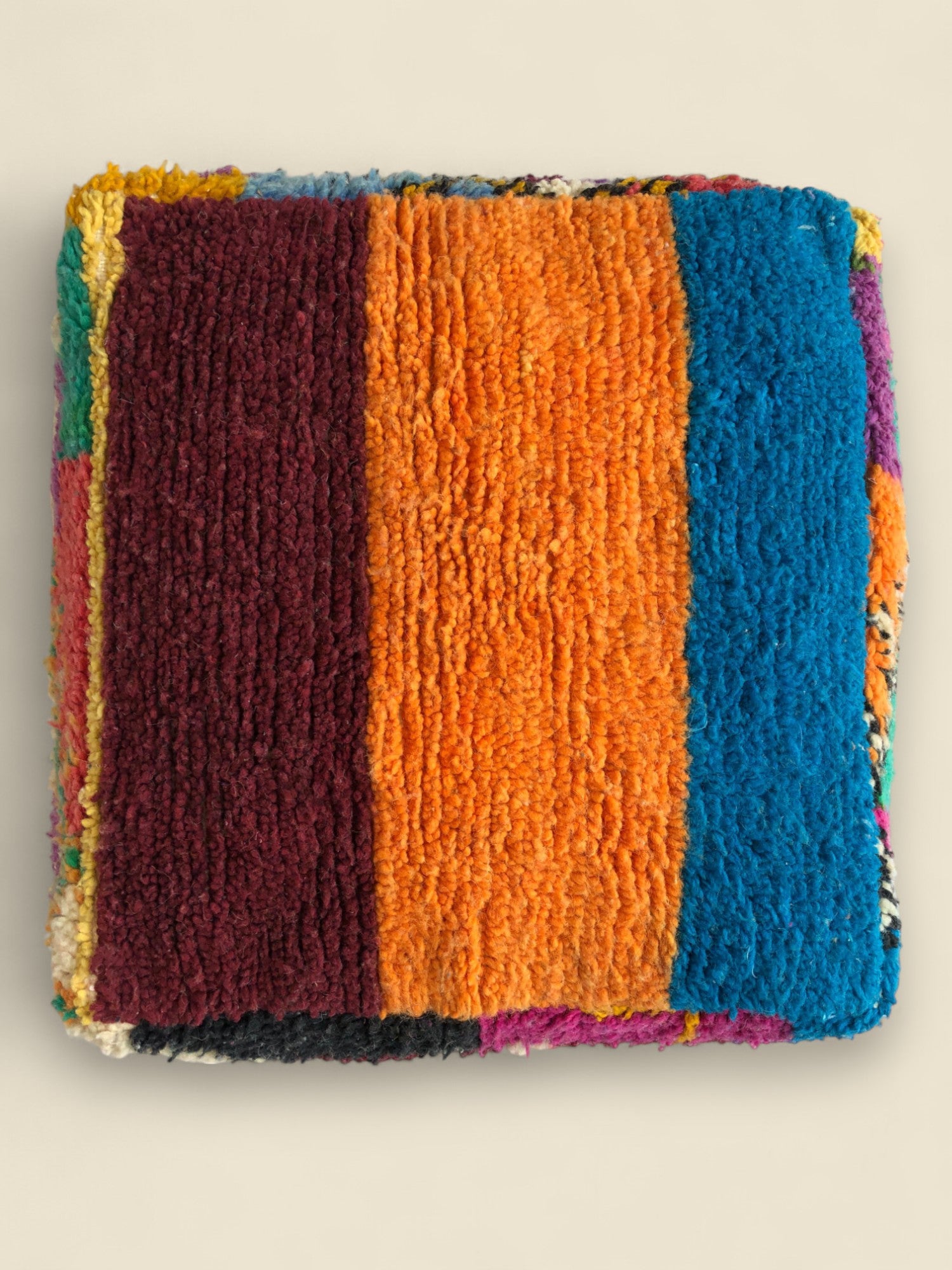 Top view of Asmoun Moroccan pouffe with vibrant orange, blue, and burgundy wool panels