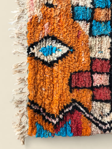 Colorful woven rug with geometric patterns and fringe on a neutral background