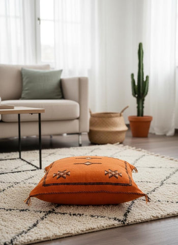 Handmade burnt orange Sabra cushion placed on neutral textured rug.