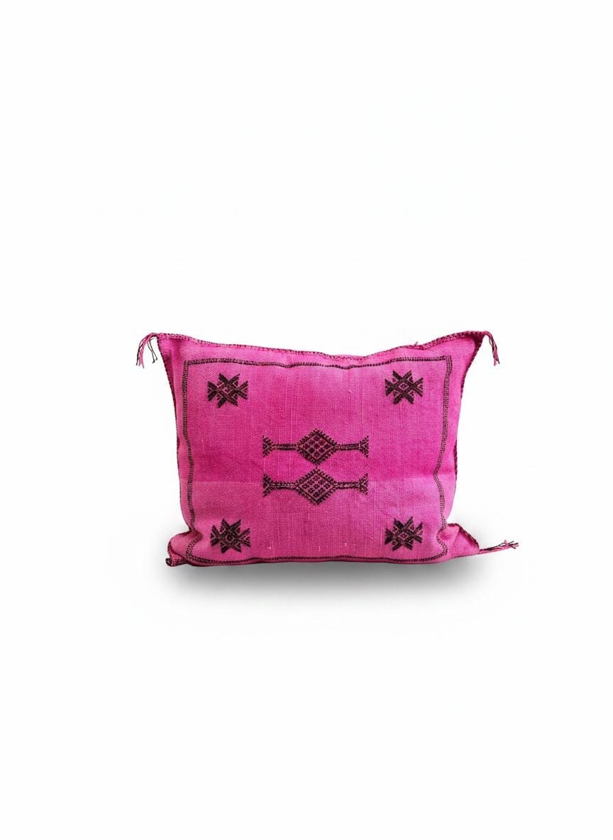 Vibrant pink Moroccan throw pillow with black geometric embroidery isolated on a clean white background.