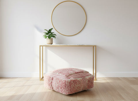 Pink Berber pouf styled under a console table in a bright minimalist room.