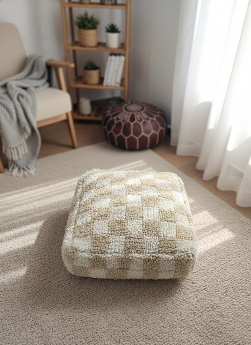 “Beige and white check pouffe on rug in bright living space.”