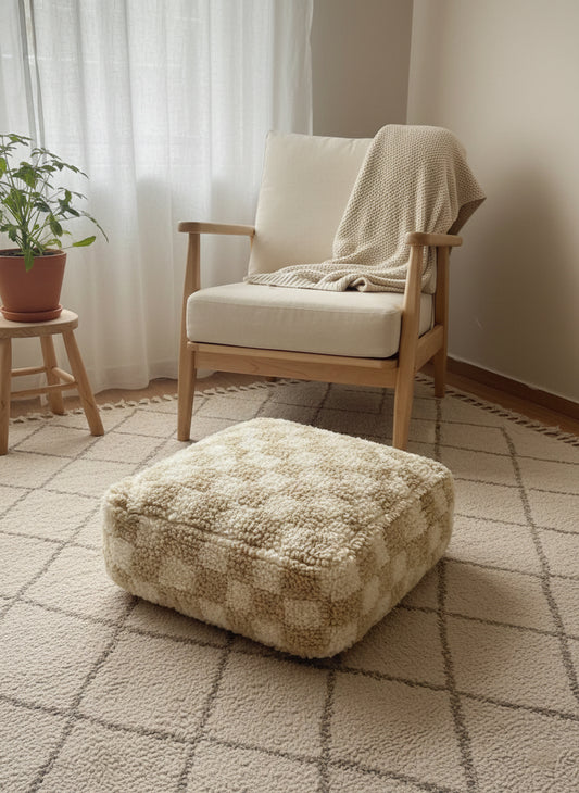 “Beige wool checkered pouffe beside armchair in cozy room.”