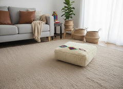 Cream wool Amnay pouf beside sofa and baskets.
