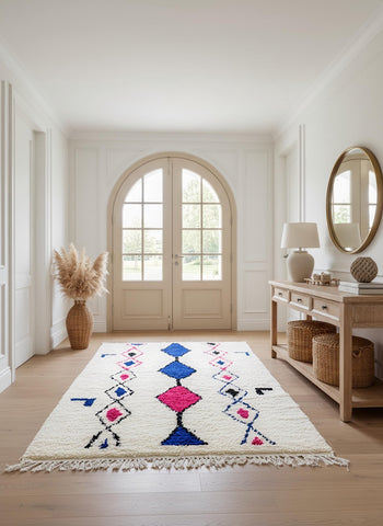 Cream Moroccan rug with tribal diamond motifs in blue and pink placed in a bright entryway with wooden console.