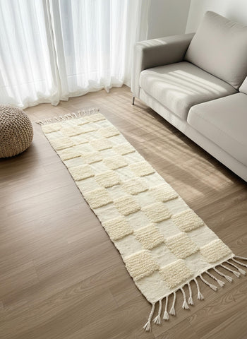 Cream Berber runner rug with raised geometric texture placed beside a beige sofa in a sunlit living room.
