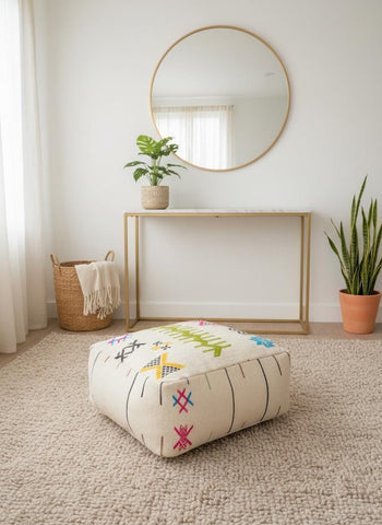 Handmade ivory Moroccan pouf with colorful geometric embroidery in a warm boho living room.