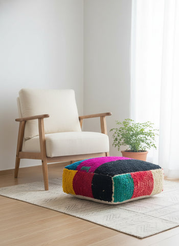 Colorful patterned ottoman in front of a white armchair in a room with a plant and rug.