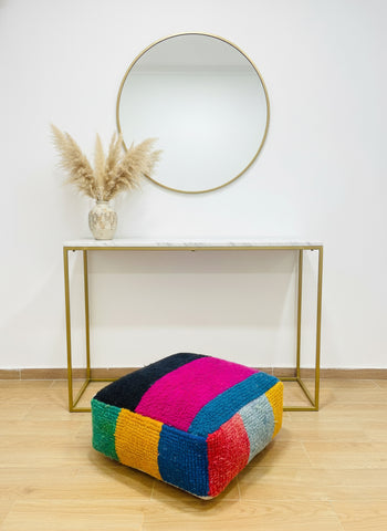 Colorful patchwork ottoman in front of a gold console table with a mirror and vase.