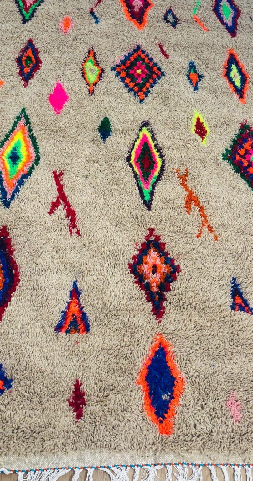 Cream Moroccan shag rug with colorful diamond motifs in neon pink, blue, orange, and green with fringe detail.