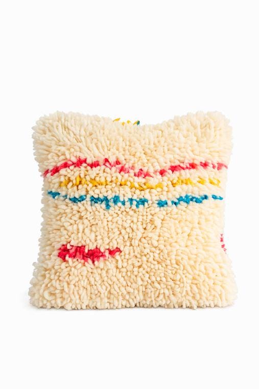 Close-up of a handmade Moroccan Berber wool pillow with colorful pink, yellow, and blue tribal accents on a white background.