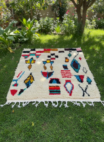 Authentic handmade wool rug with bold abstract Berber symbols displayed on lush green grass.