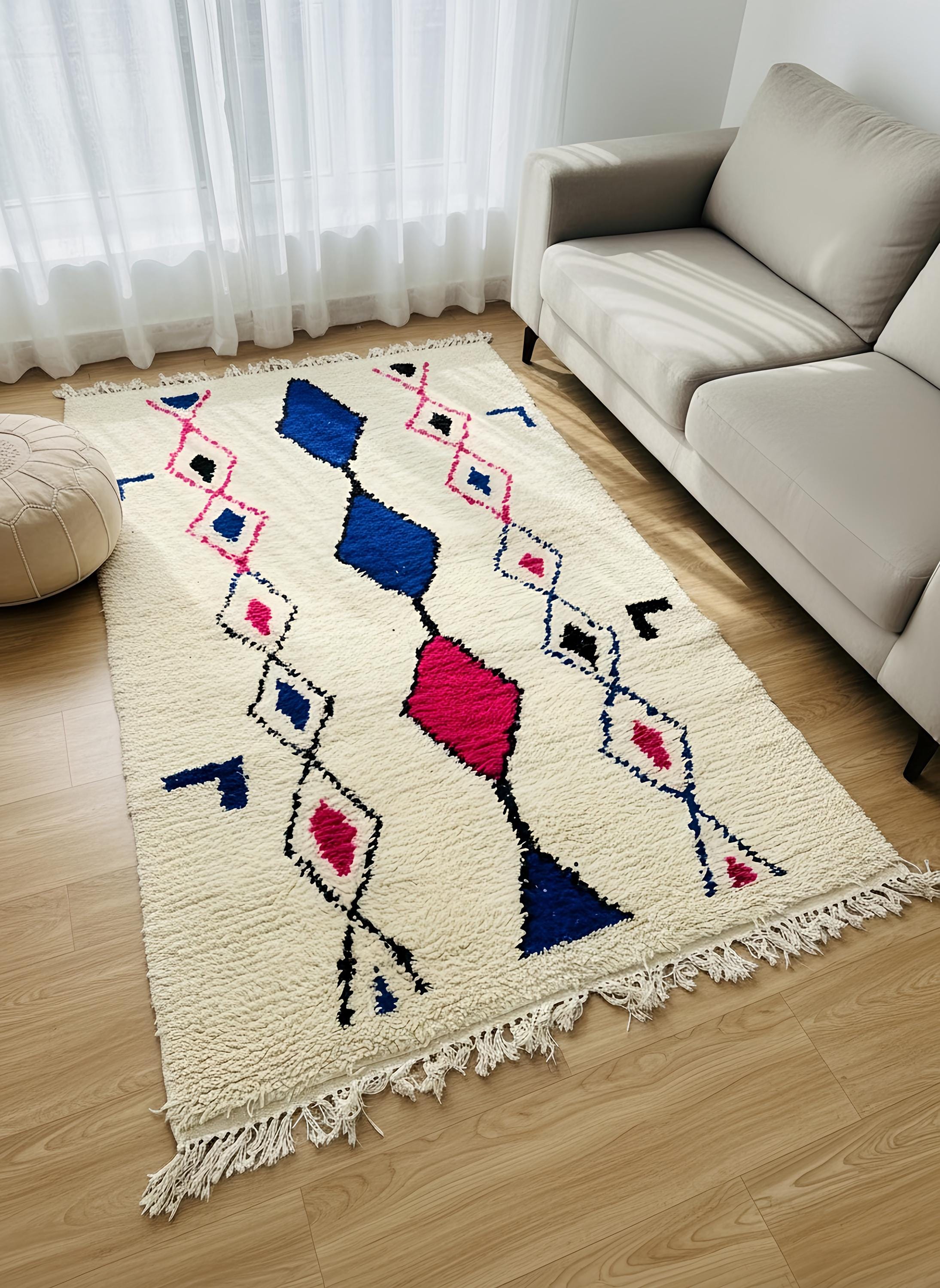 Soft ivory Berber rug with blue and pink geometric details placed beside a sofa in a sunlit space.