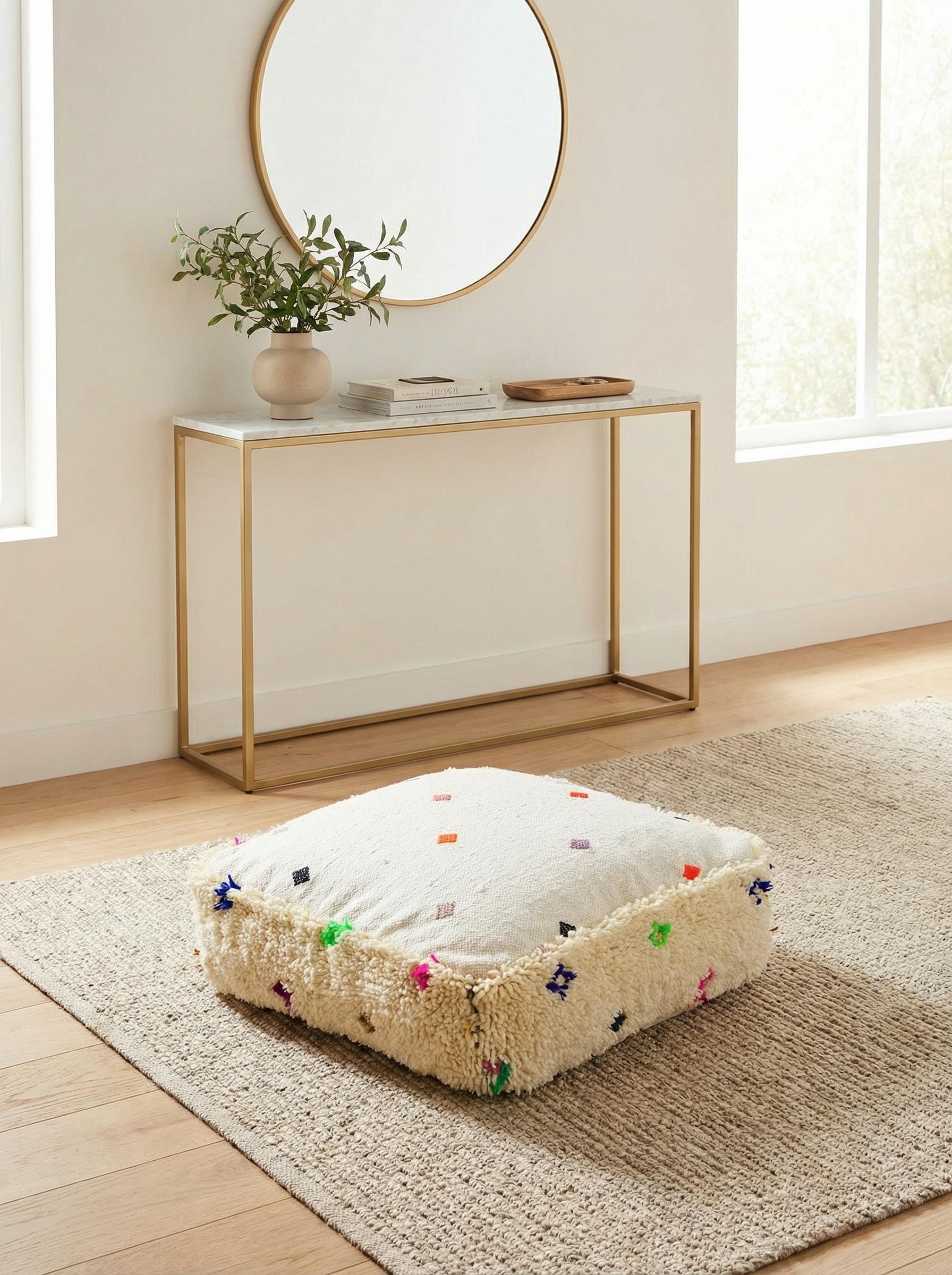 Handmade cream wool pouf placed on rug under modern console and round mirror
