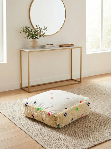 Handmade cream wool pouf placed on rug under modern console and round mirror