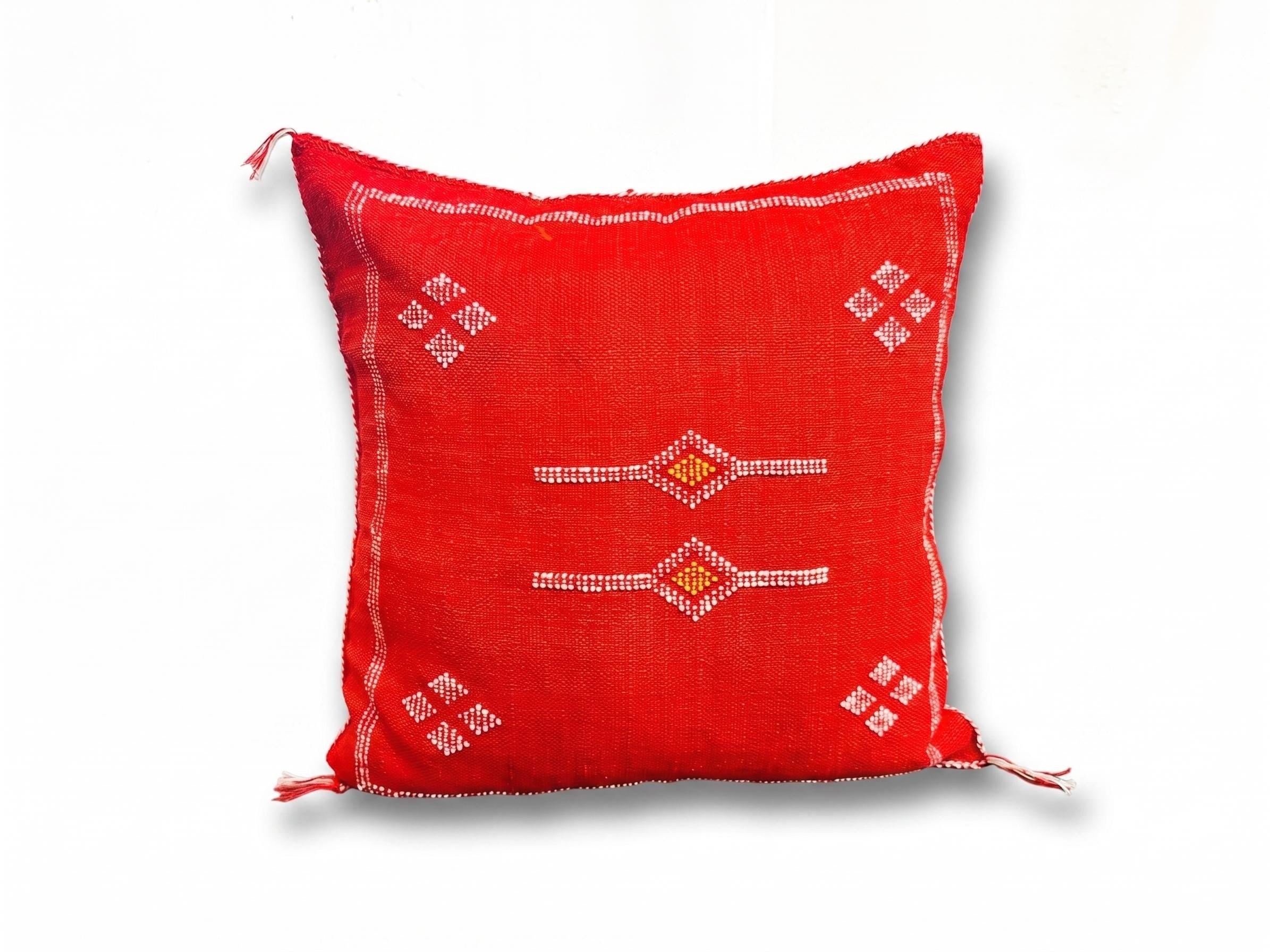 Authentic Moroccan red pillow cover with geometric embroidery and decorative tassel corners on a textured rug.
