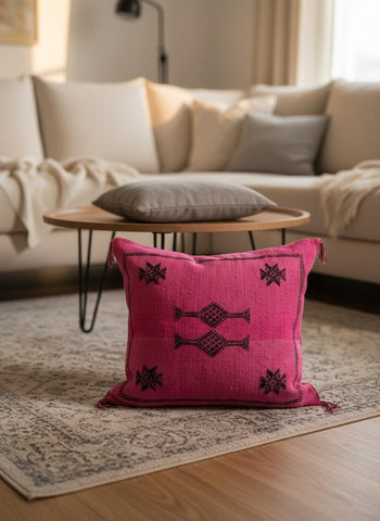 Bright pink Moroccan cactus silk pillow with black tribal embroidery styled in a cozy modern living room.