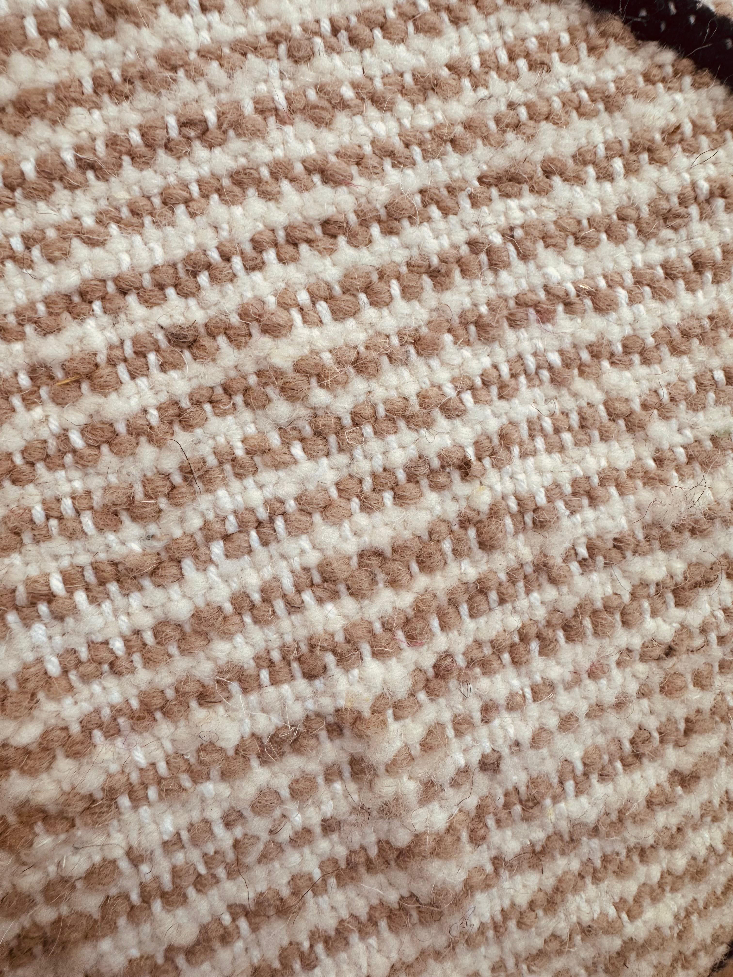 Close-up texture of handwoven beige and cream wool fabric from the pouf