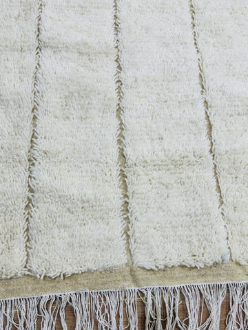 Close-up of Tazgart cream wool rug with raised linear texture and fringe edges.