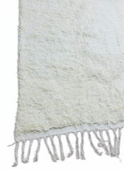 Detailed view of soft beige wool rug surface and handwoven fringe