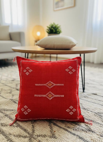 Handcrafted red Sabra pillow with white embroidered details displayed in a warm, modern living space.