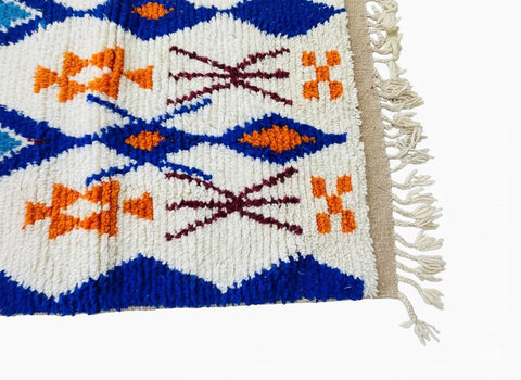 Colorful Moroccan runner rug with blue and orange geometric motifs on a cream background, finished with hand-knotted fringe.