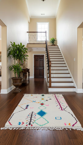 “Tasga Moroccan Berber rug placed in a hallway entry with wooden stairs and indoor plants.”