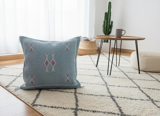 Blue Moroccan cactus silk pillow styled on cream Berber rug with coffee table