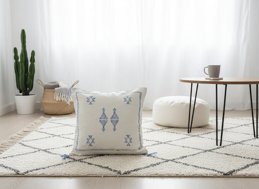 Handwoven Moroccan Tilya Berber pillow in cream and blue with tribal pattern on rug
