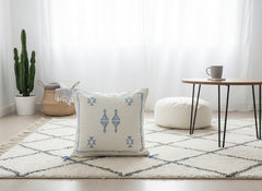 Handwoven Moroccan Tilya Berber pillow in cream and blue with tribal pattern on rug