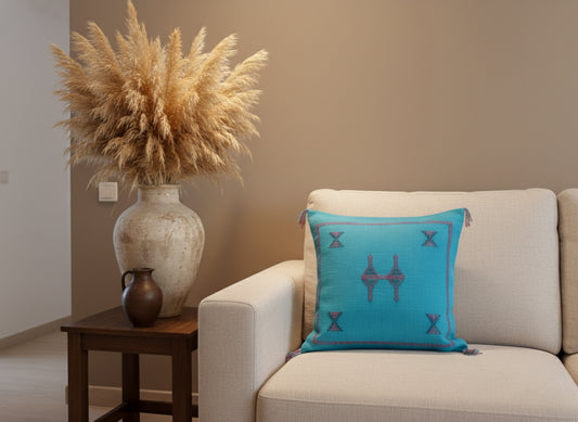 Handmade Tasga Berber pillow in turquoise with geometric embroidery on beige sofa