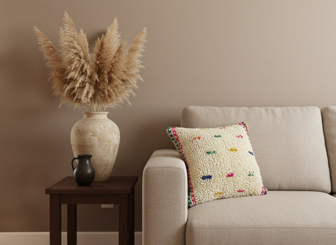 Decorative pillow on a couch next to a vase with pampas grass against a beige wall.