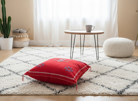 Red Moroccan Tisri rug pillow with tribal embroidery on a neutral Berber rug in a bright living room.