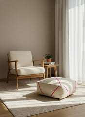 Wool pouf with pink lines beside armchair in natural light