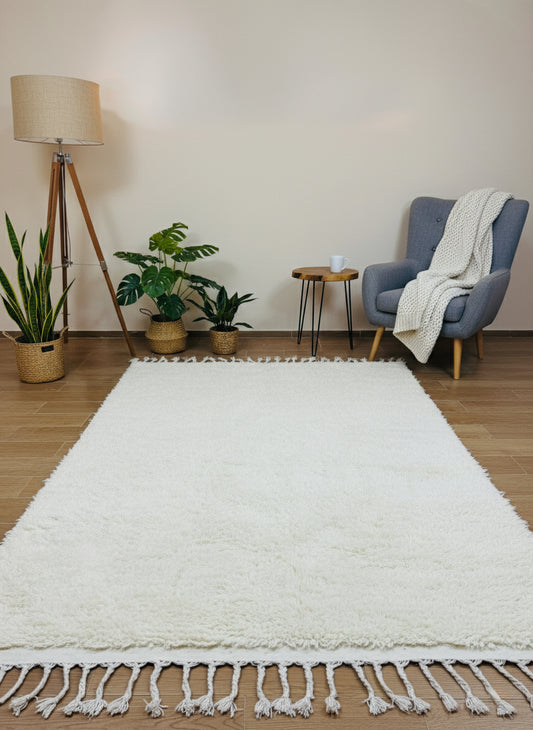 Minimalist beige wool rug with fringe styled beside armchair and plants