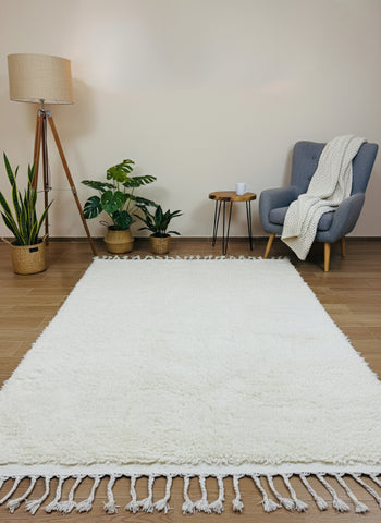 Minimalist beige wool rug with fringe styled beside armchair and plants