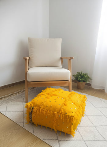 Handmade yellow Berber pouf with fringes and sequins placed in a modern living room.
